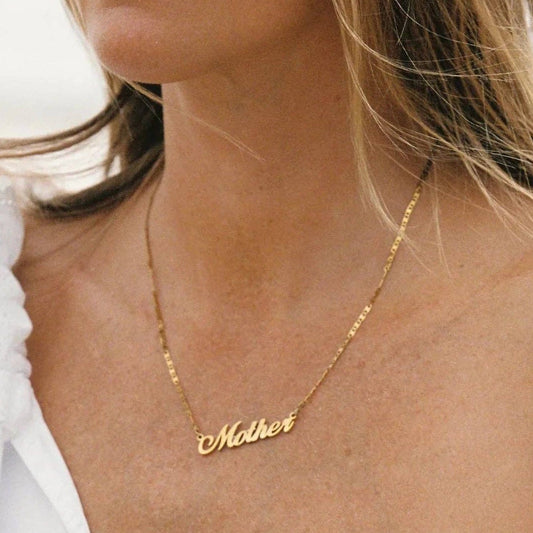 A close-up lifestyle shot of a woman wearing a delicate gold chain necklace with the word 'Mother' written in cursive script on the pendant.