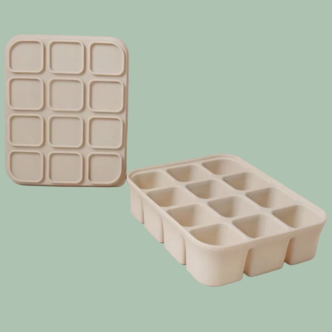 Two off-white silicone ice cube trays, one standing upright and one lying flat, shown on a neutral beige and pink studio background.