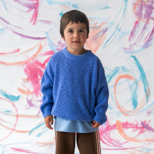 Child wearing a blue sweater standing in front of a colorful abstract wall.