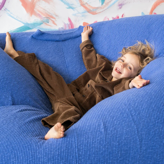 Child in brown outfit lying on a blue bean bag chair with colorful wall art in the background