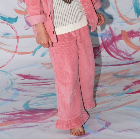 Person wearing pink corduroy pants and a matching jacket on a colorful abstract background