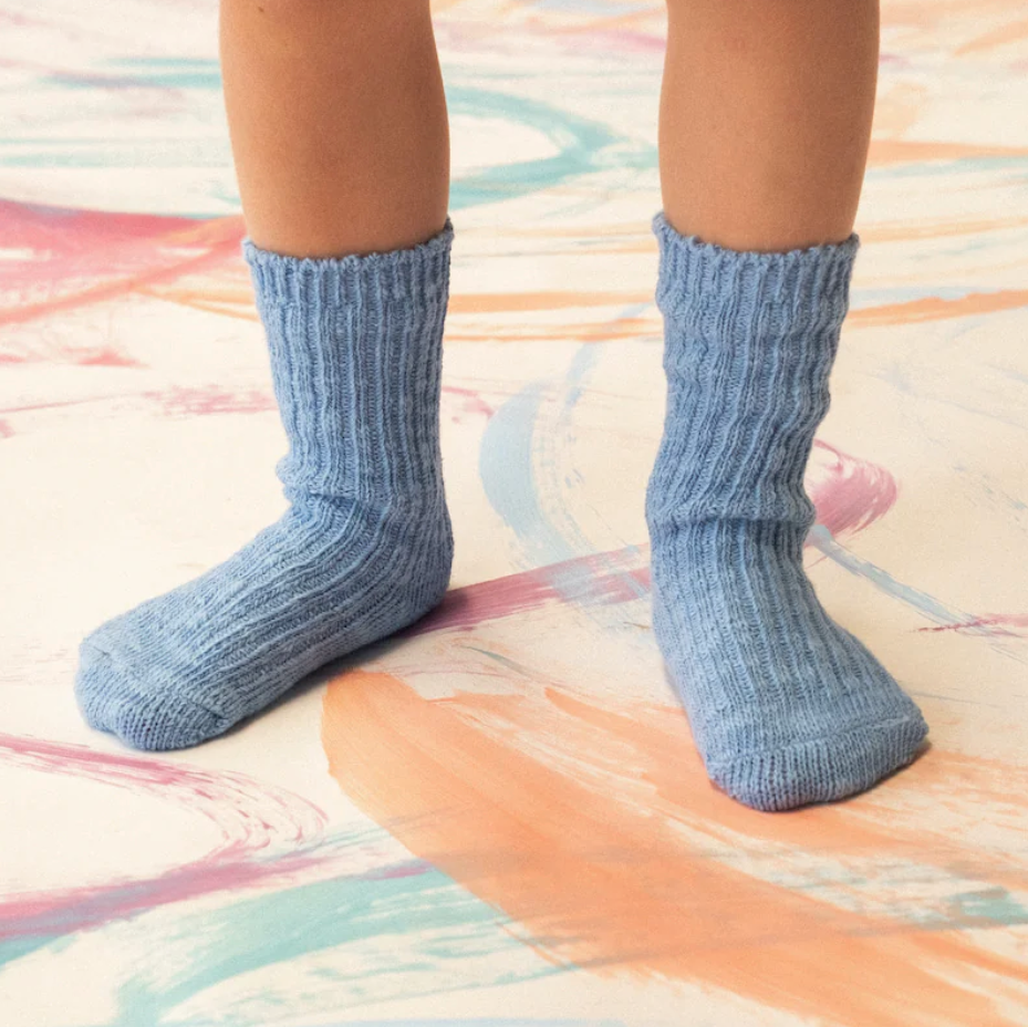 Blue knitted socks on a child's feet with a colorful carpet background