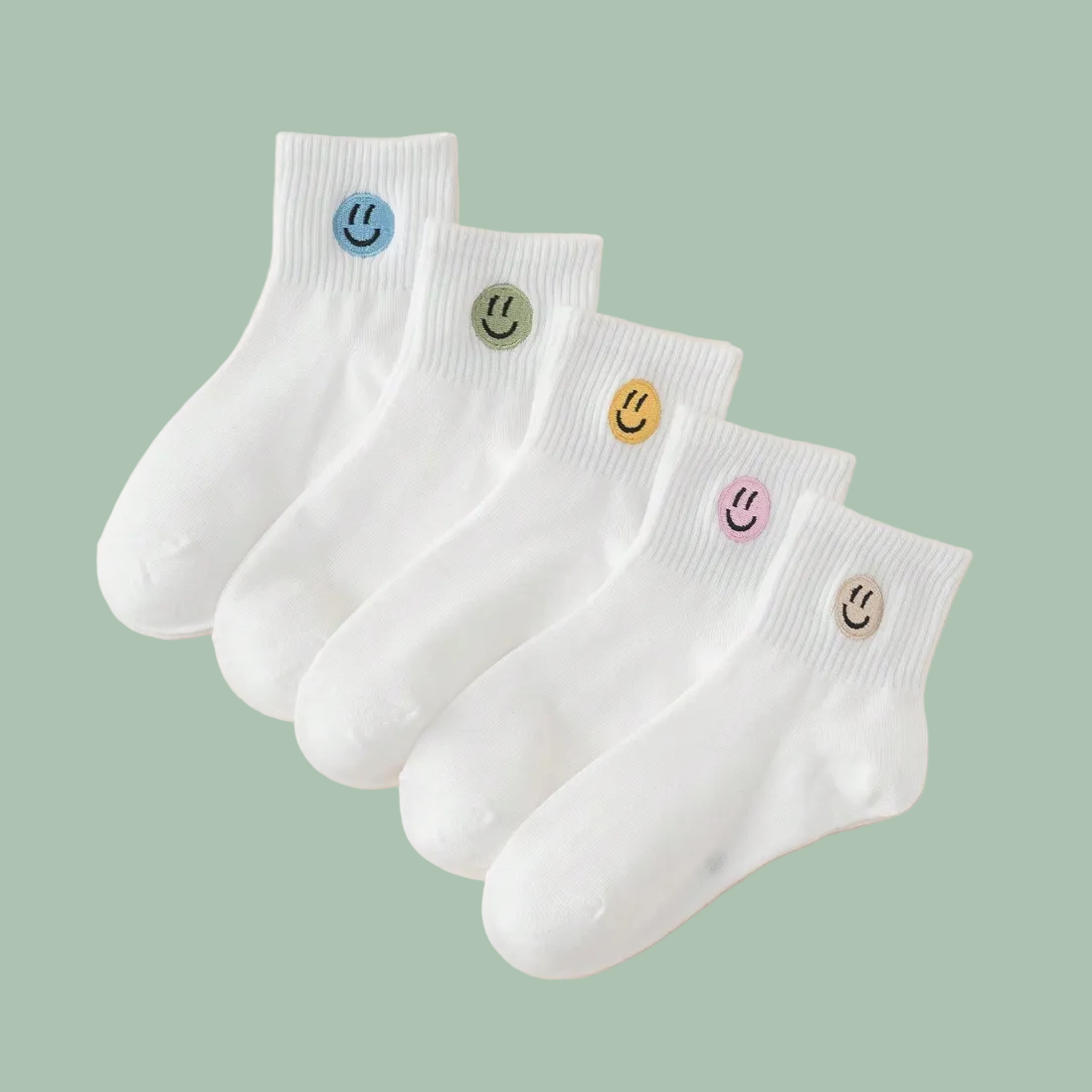 Five pairs of white ankle socks arranged in a fan shape on a light beige background. Each sock has a small embroidered smiley face in a different color: blue, green, yellow, pink, and brown.