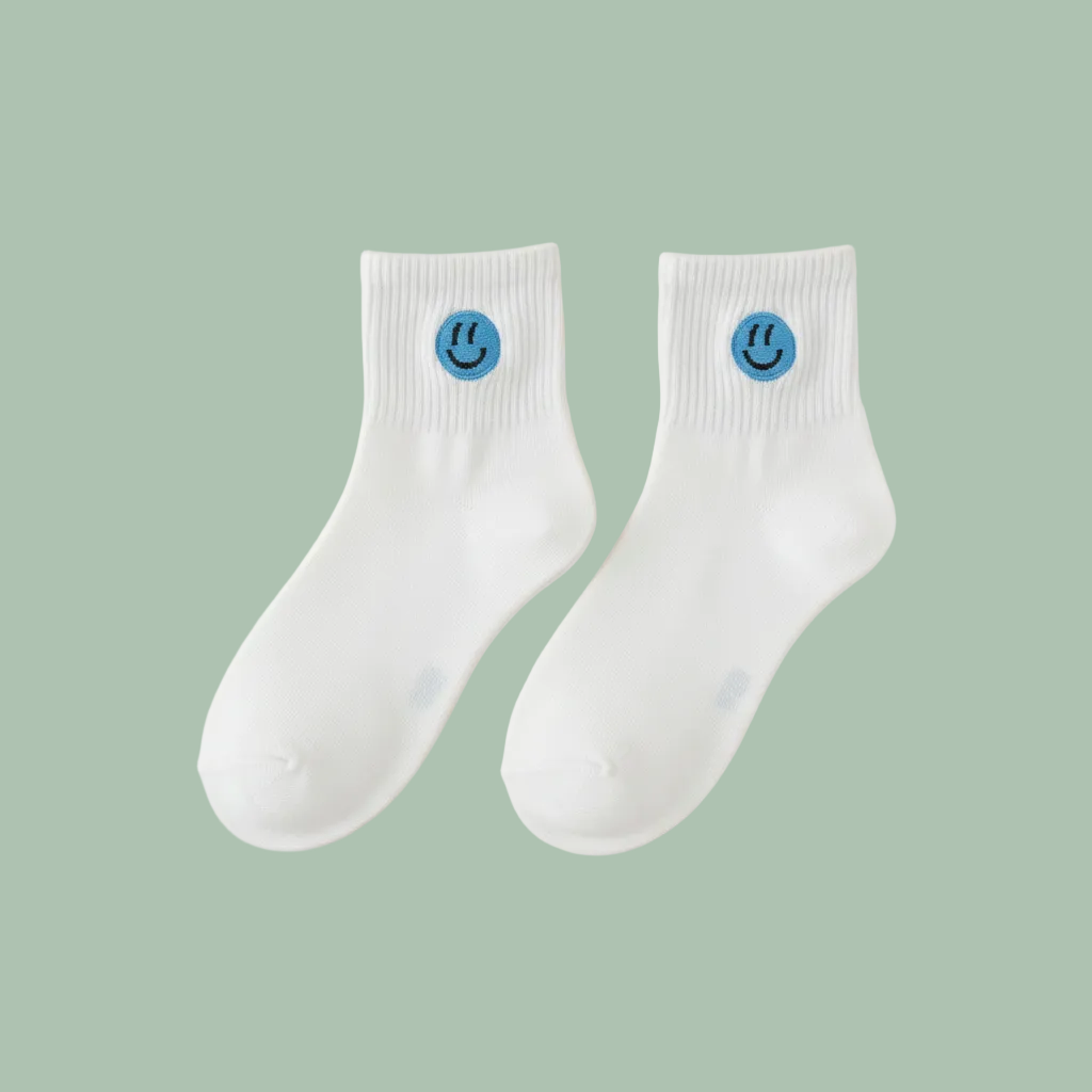 A pair of white ankle socks with a small blue smiley face logo on the cuff, displayed on a light beige background.