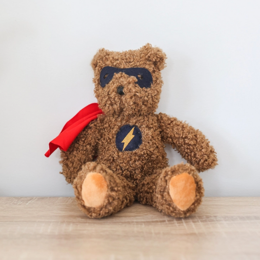 Teddy bear with superhero cape and mask on a wooden surface
