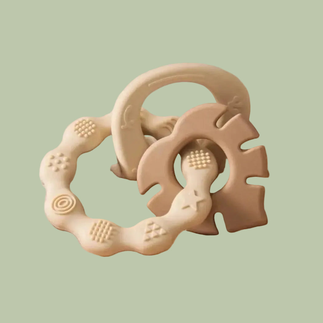 Beige baby teething ring on a wooden surface with white fabric in the background
