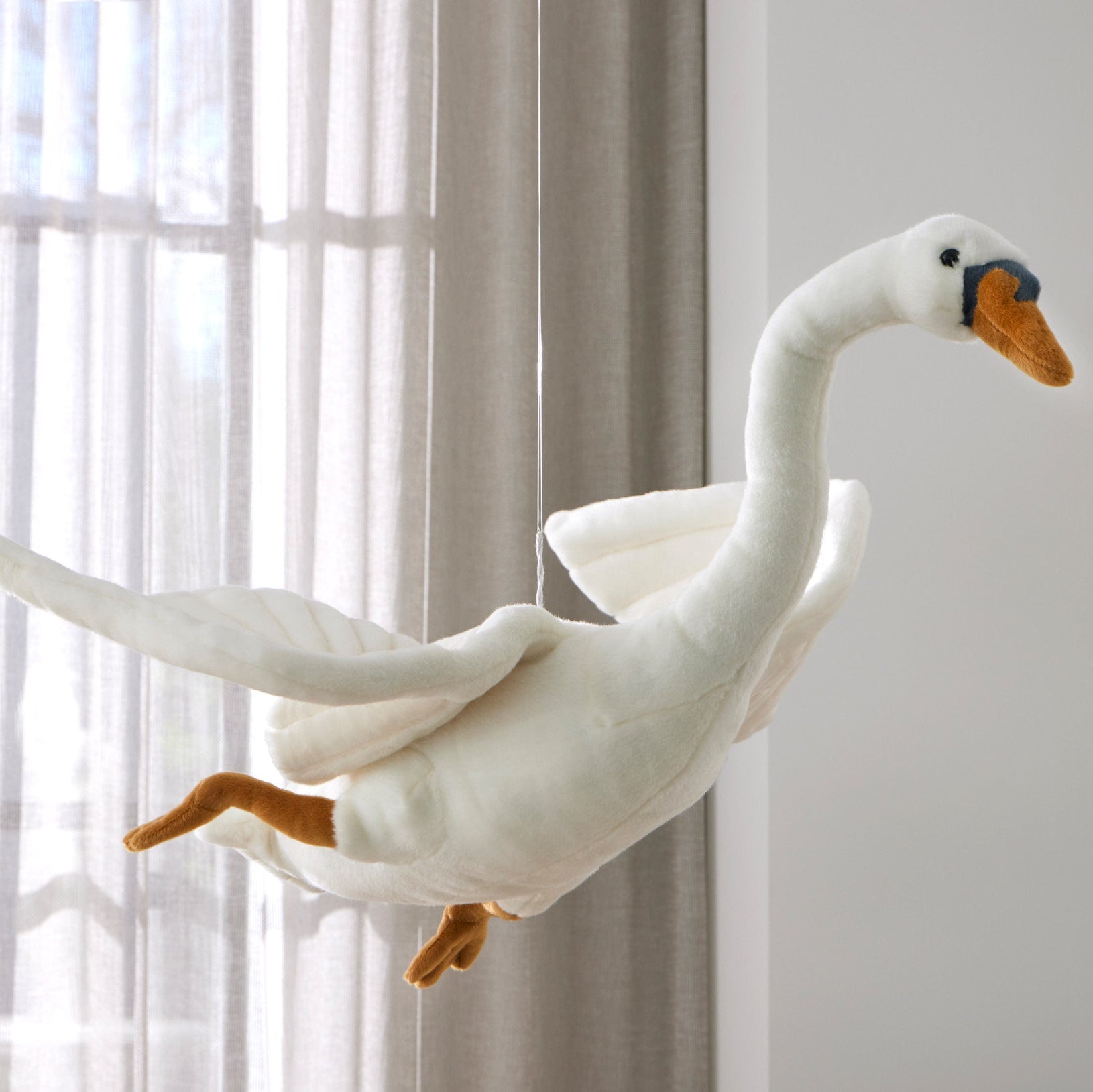 Plush swan toy in a room with curtains and a light background