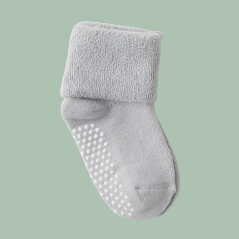 A pair of light gray fuzzy baby socks with white grip dots on the sole, shown on a clean white background with a second white sock partially visible on the right.