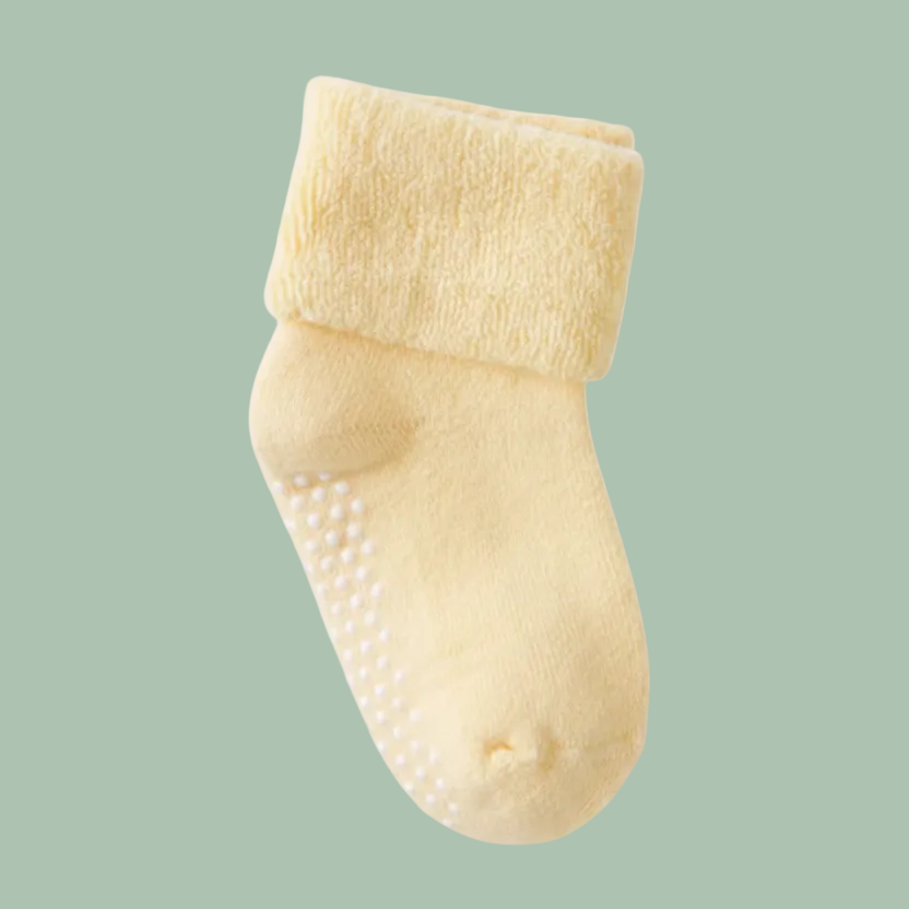 A pale yellow baby sock with white non-slip grip dots on the sole