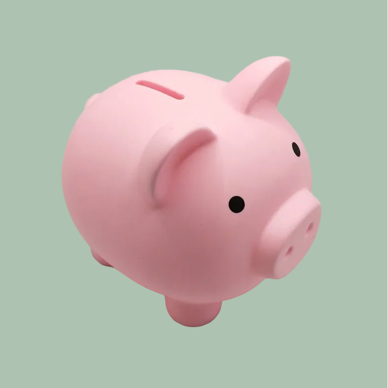 A classic pink ceramic piggy bank with small black eyes, set against a solid sage green background.