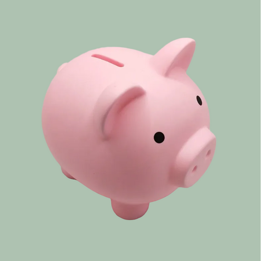 A classic pink ceramic piggy bank with small black eyes, set against a solid sage green background.