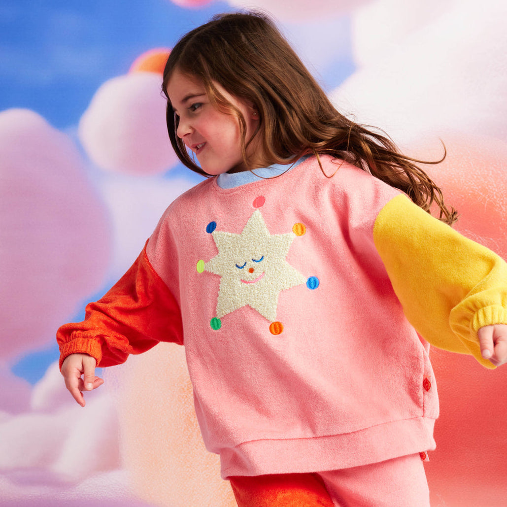 Child wearing a colorful outfit with star designs on a soft, cloud-like background