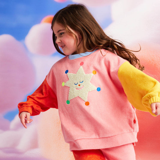Child wearing a colorful outfit with star designs on a soft, cloud-like background
